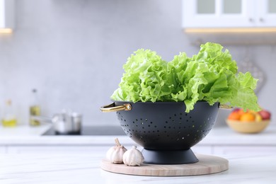 Photo of Fresh lettuce in black colander on white marble table in kitchen. Space for text