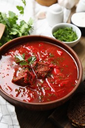 Photo of Stylish brown clay bowl with Ukrainian borsch served on wooden table