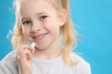 Photo of Little girl taking vitamin pill on light blue background, closeup