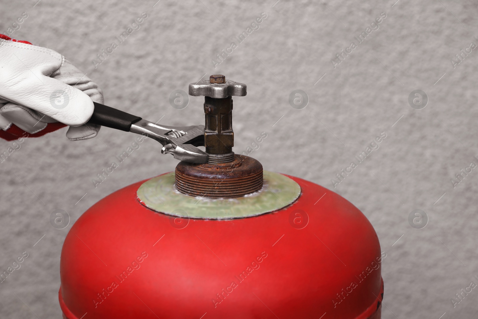 Photo of Worker with adjustable wrench opening red gas cylinder near wall, closeup