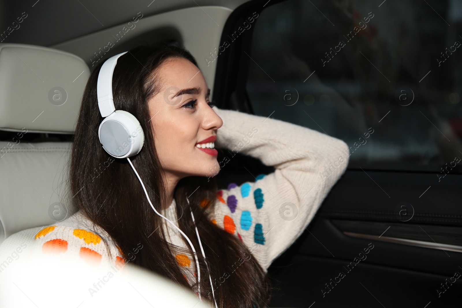 Photo of Beautiful young woman listening to music with headphones in car. Space for text