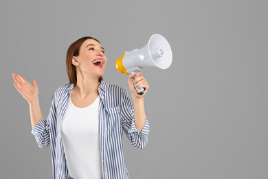 Emotional young woman with megaphone on light grey background. Space for text