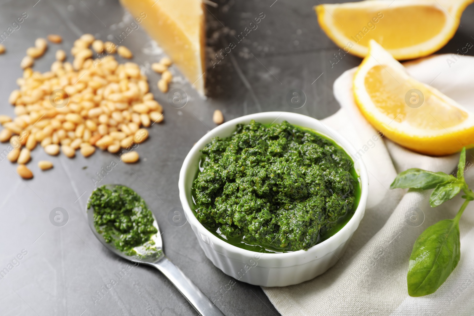 Photo of Bowl and spoon with basil pesto sauce on table