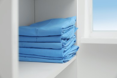 Photo of Light blue medical uniforms on white rack indoors, space for text