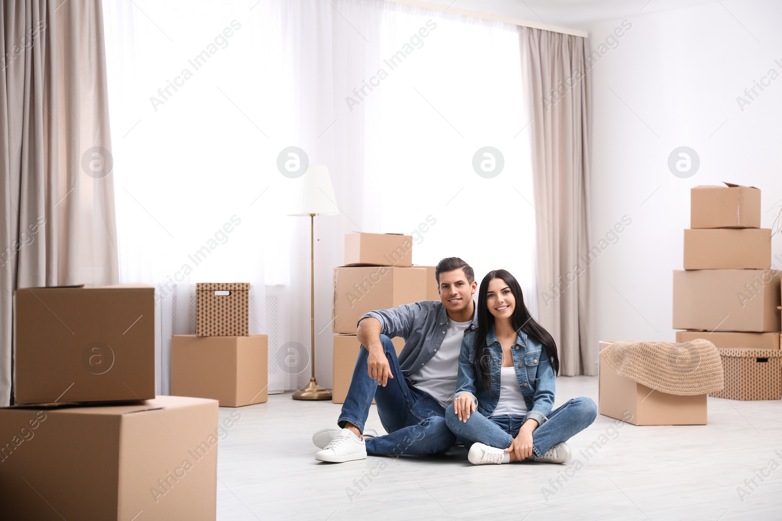 Photo of Happy couple in room with cardboard boxes on moving day