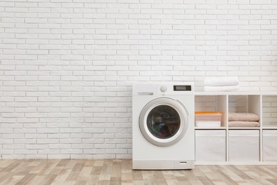 Photo of Modern washing machine near brick wall in laundry room interior, space for text