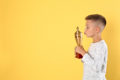 Photo of Happy boy with golden winning cup on yellow background. Space for text