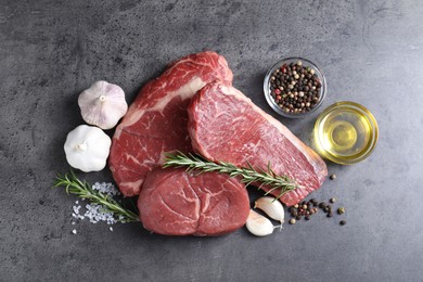 Photo of Raw beef steaks, oil and spices on grey table, flat lay