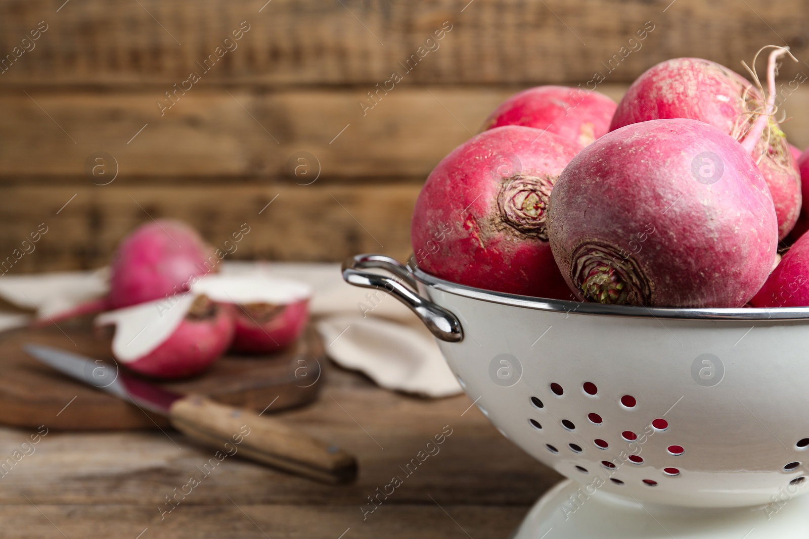 Photo of Colander with red turnips on wooden table, closeup. Space for text