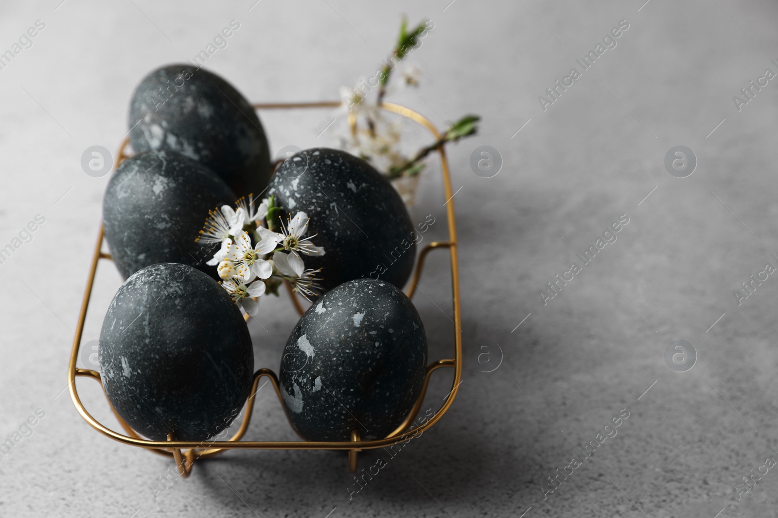 Photo of Decorated Easter eggs and flowers on grey table, closeup. Space for text