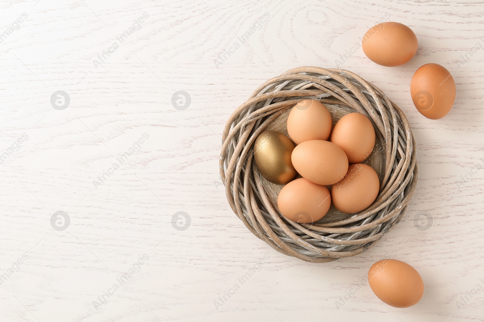 Photo of Golden egg among others in nest on wooden background, top view with space for text