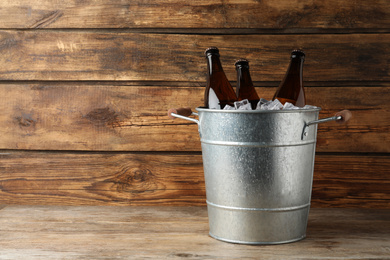 Photo of Metal bucket with beer and ice cubes on wooden background. Space for text