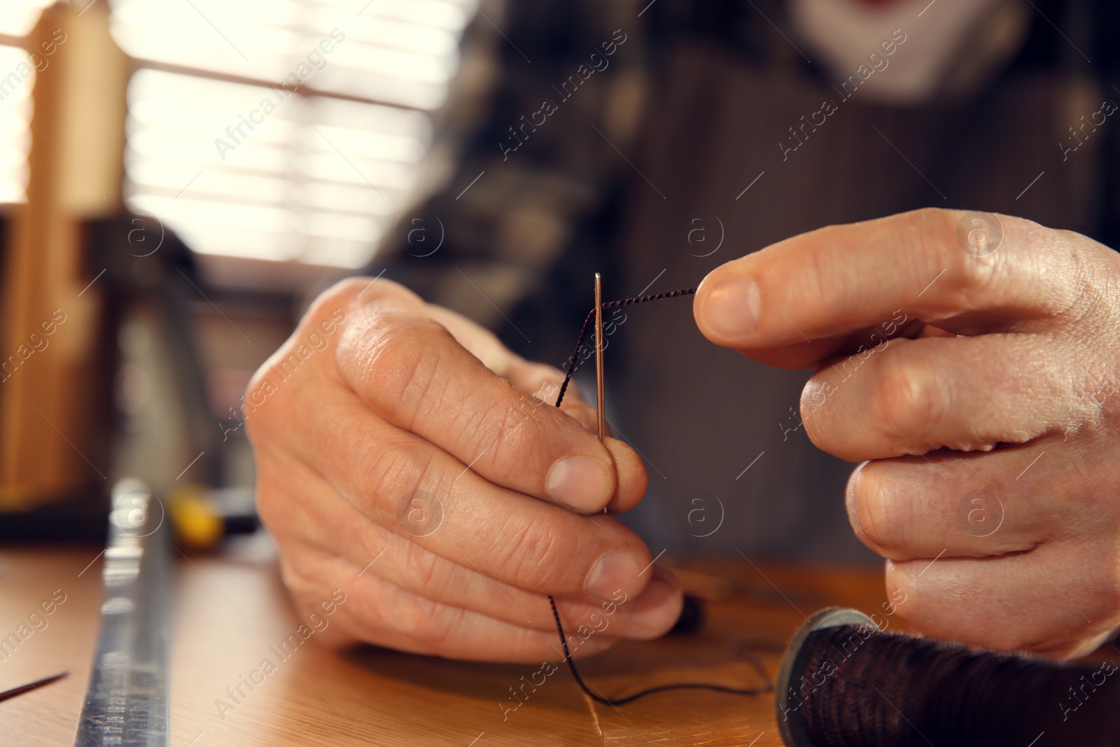 Photo of Man threading needle for leather working, closeup