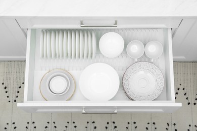 Open drawer with different plates and bowls in kitchen, above view