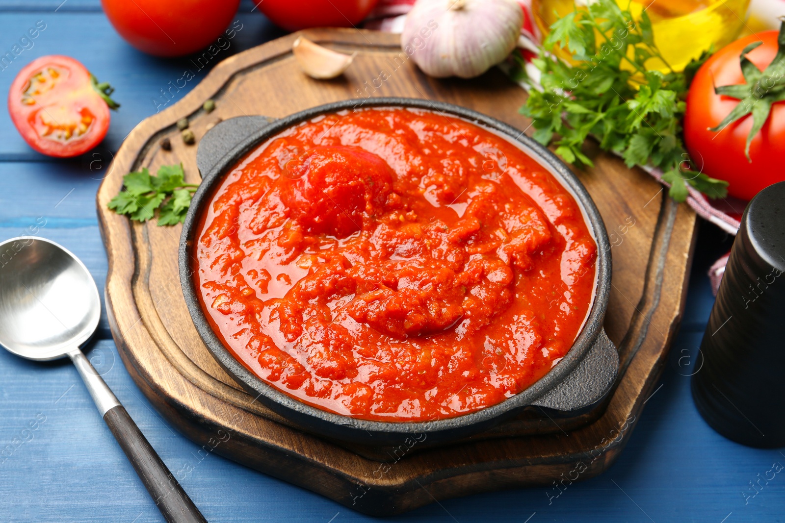 Photo of Homemade tomato sauce in bowl, spoon and ingredients on blue wooden table