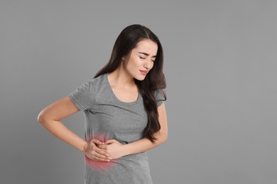 Young woman suffering from liver pain on grey background