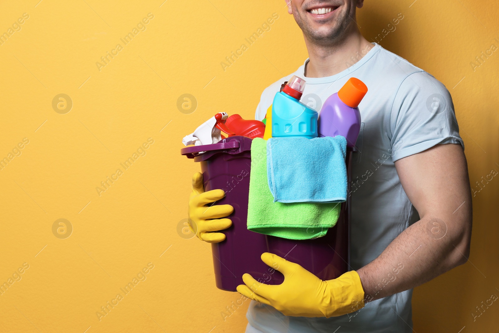 Photo of Man with bucket of detergents on color background, closeup. Space for text