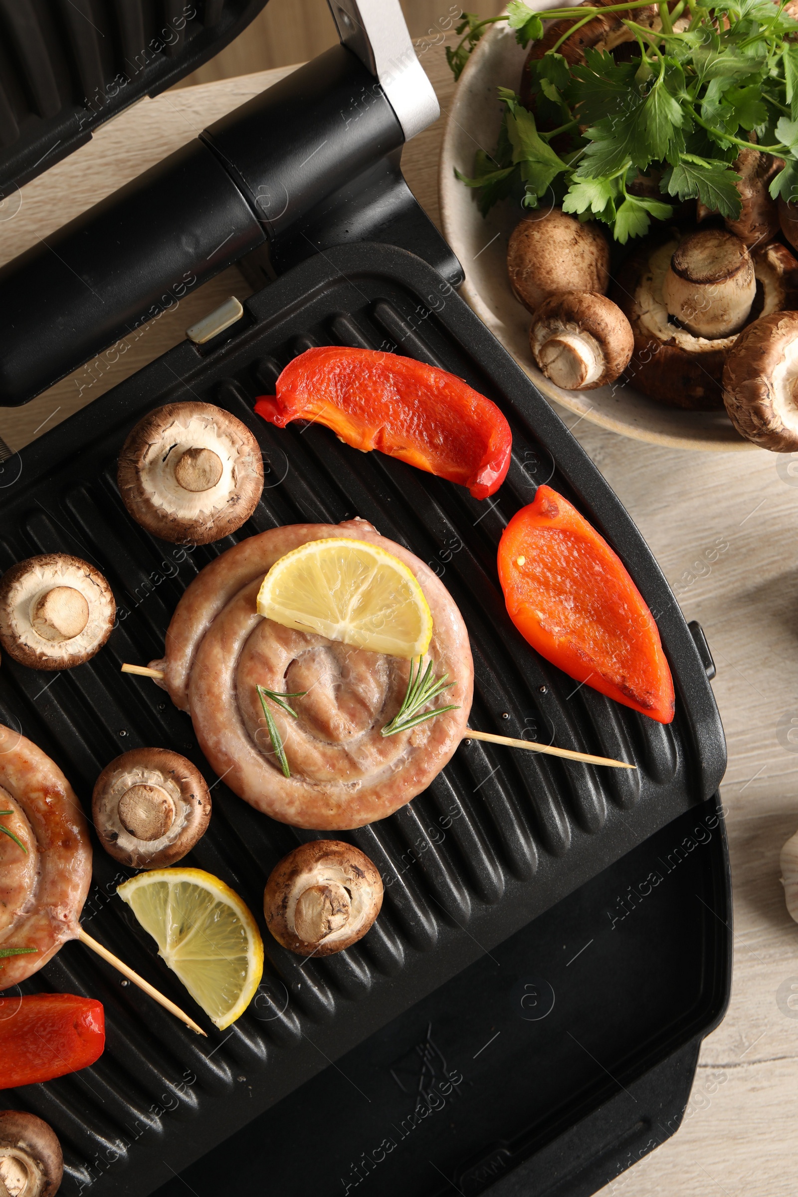 Photo of Electric grill with homemade sausages, mushrooms and bell pepper on table, flat lay