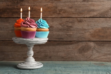Photo of Stand with delicious birthday cupcakes with burning candles on table