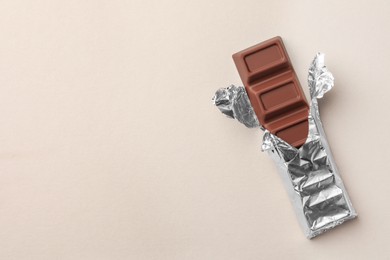 Photo of Tasty chocolate bar wrapped in foil on light background, top view. Space for text