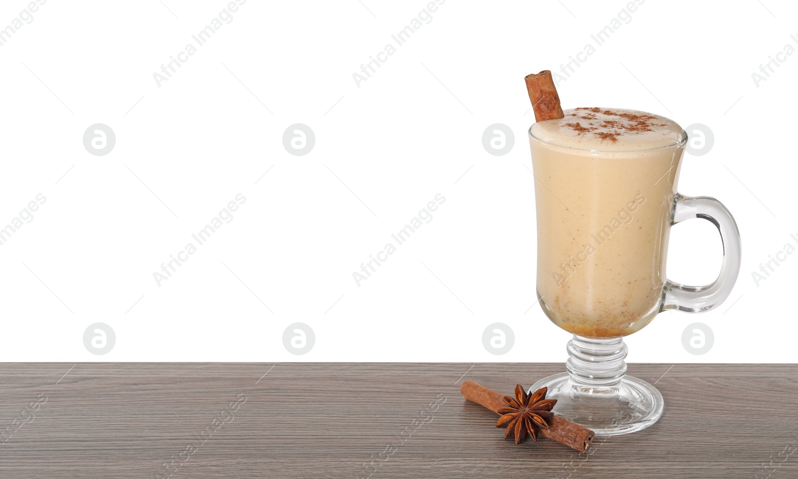 Photo of Delicious eggnog in glass, anise and cinnamon sticks on wooden table against white background, space for text