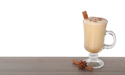 Photo of Delicious eggnog in glass, anise and cinnamon sticks on wooden table against white background, space for text