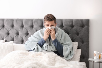 Photo of Sick young man with tissue suffering from cold in bed