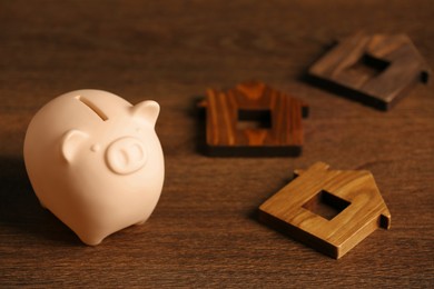 Photo of Piggy bank and house models on wooden table. Space for text