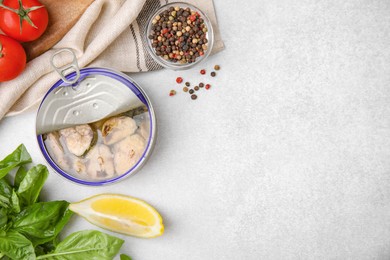 Open tin can with mackerel chunks, spices and tomatoes on grey table, flat lay. Space for text