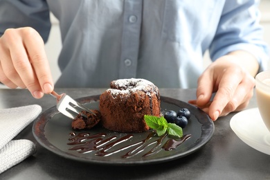 Photo of Woman eating delicious fresh fondant with hot chocolate at table. Lava cake recipe