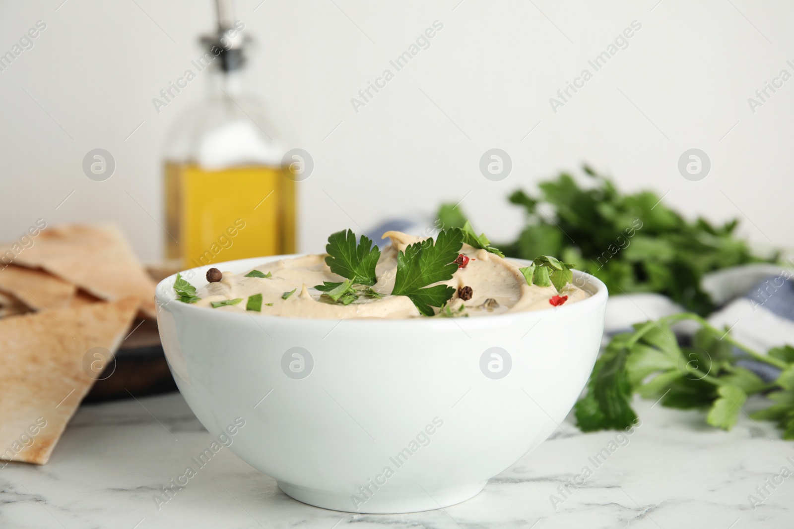 Photo of Delicious hummus with parsley and pita chips on white marble table, closeup