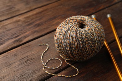 Photo of Soft woolen yarn and knitting needles on wooden table, space for text
