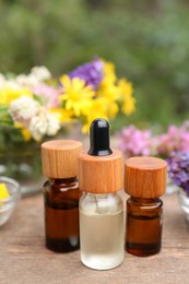 Bottles of essential oils and many beautiful flowers on wooden table