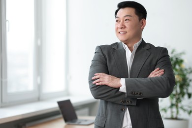 Portrait of smiling businessman with crossed arms in office. Space for text