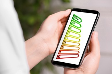 Energy efficiency. Woman using smartphone with colorful rating on display indoors, closeup