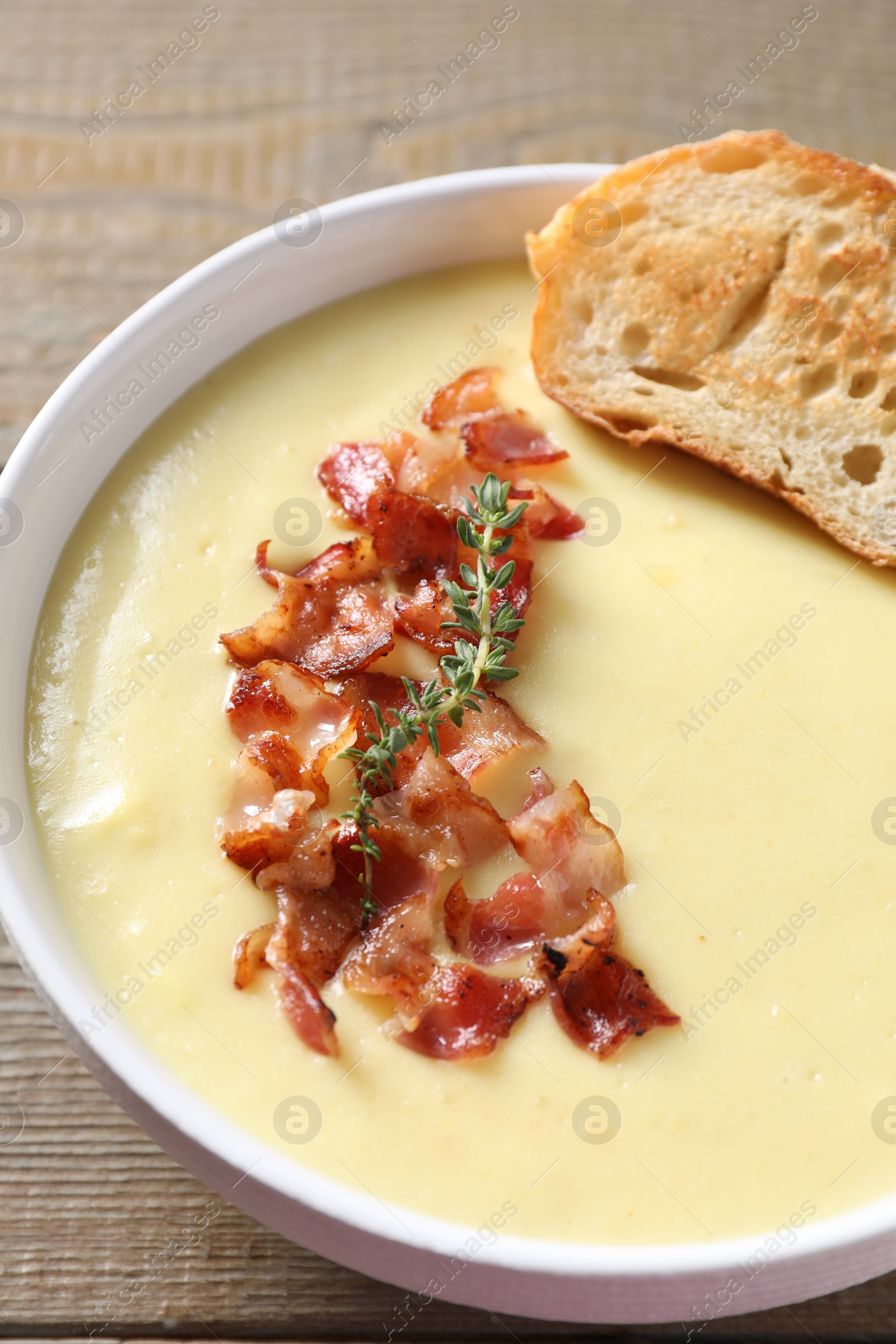 Photo of Tasty potato soup with bacon and crouton in bowl on wooden table, closeup