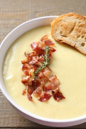 Photo of Tasty potato soup with bacon and crouton in bowl on wooden table, closeup