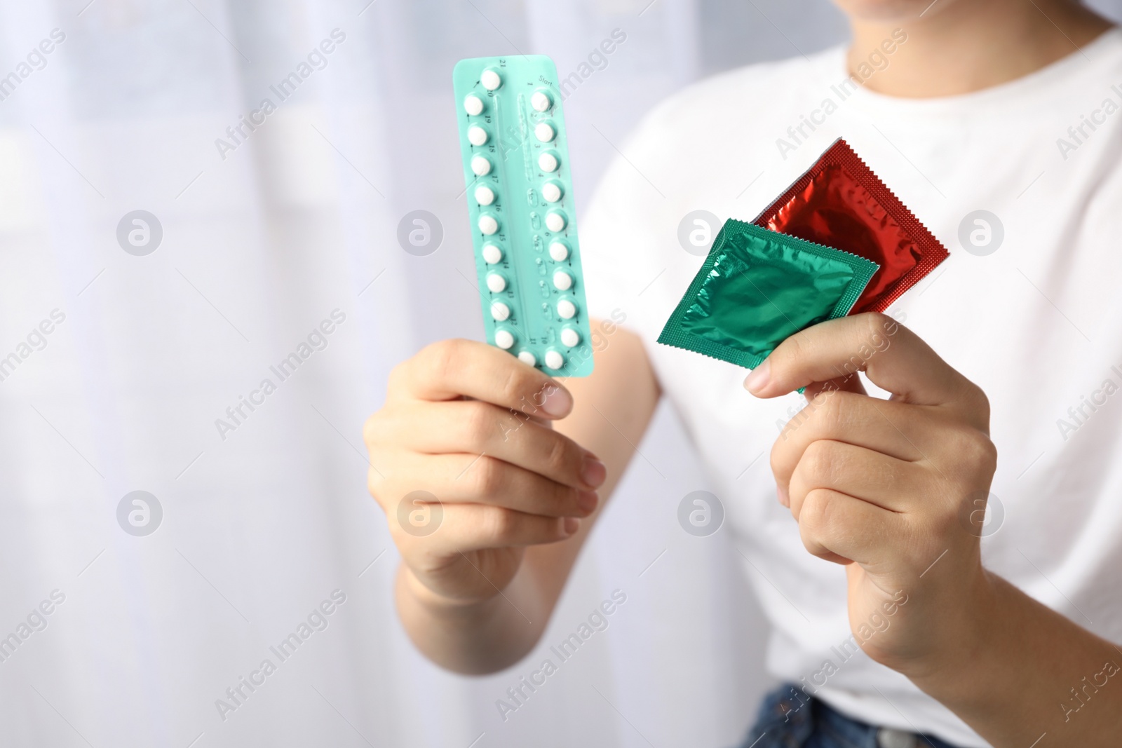 Photo of Young woman holding birth control pills and condoms on light background, closeup. Safe sex concept