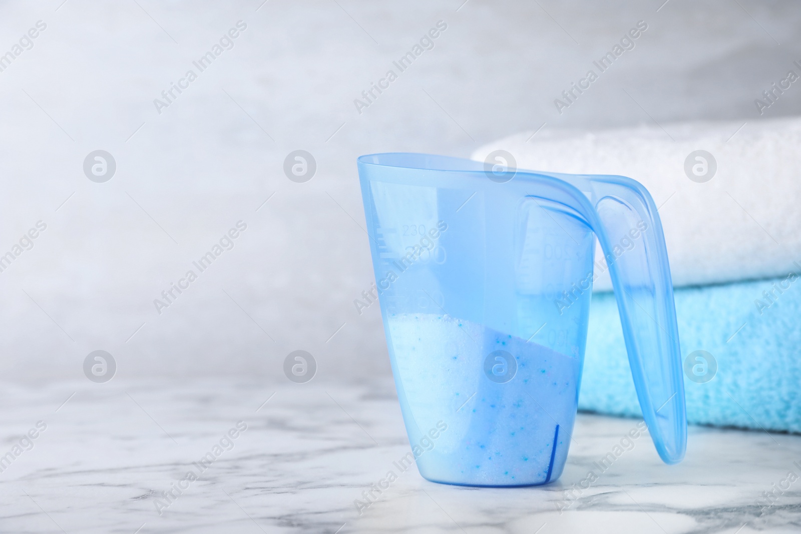 Photo of Measuring cup of laundry powder and towels on marble table, space for text