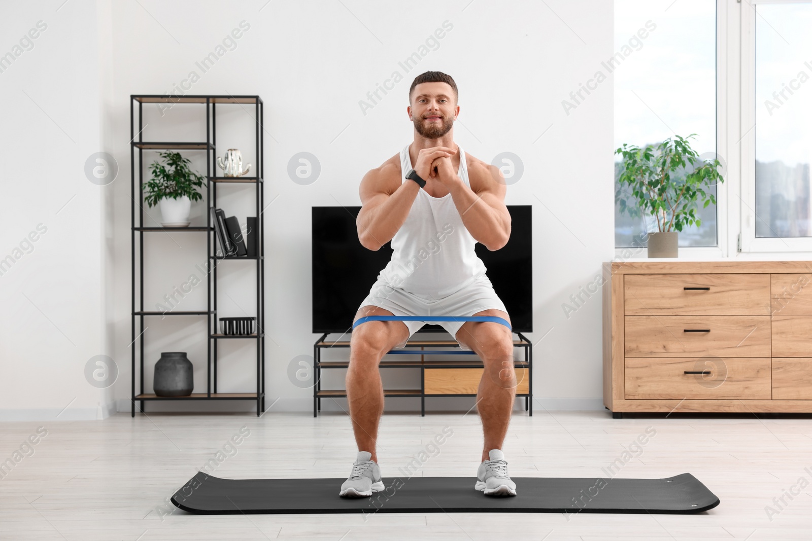 Photo of Athletic man doing exercise with elastic resistance band on mat at home