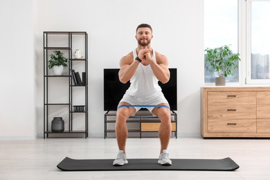 Athletic man doing exercise with elastic resistance band on mat at home