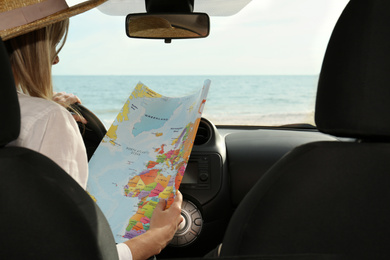 Photo of Young woman with world map in car, back view. Road trip