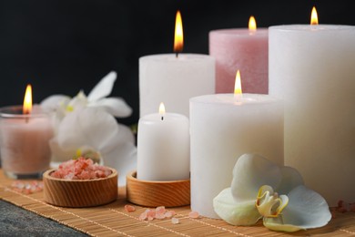 Photo of Beautiful spa composition with burning candles and flowers on dark grey table against black background