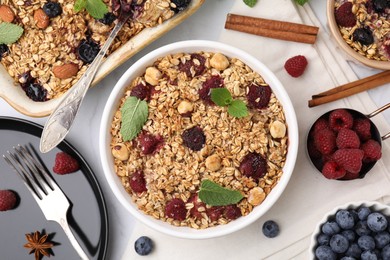 Tasty baked oatmeal with berries, nuts and cinnamon sticks on white table, flat lay