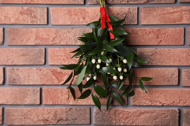 Photo of Mistletoe bunch with red ribbon hanging on brick wall. Traditional Christmas decor