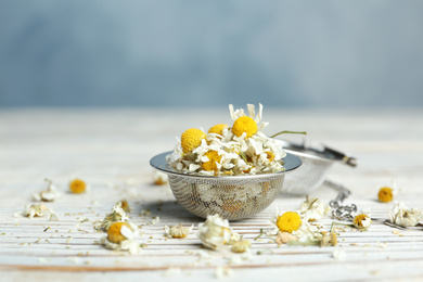 Photo of Dry chamomile flowers in infuser on white wooden table, closeup