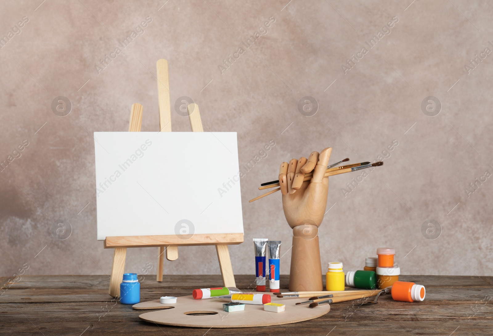 Photo of Wooden easel with blank canvas board and painting tools for children on table near color wall. Space for text