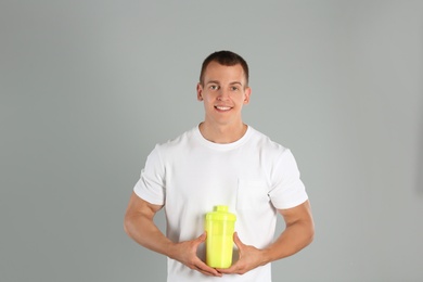 Photo of Athletic young man with protein shake on light grey background