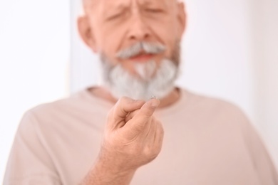 Senior man with contact lens on light background