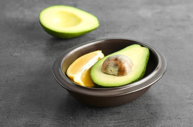 Photo of Bowl with ripe avocado and lemon on grey background